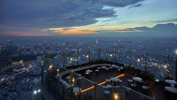 A rooftop bar with a panoramic city view, glass railings, and round tables. - Vinhomes Urban Apartment HCM (Ho Chi Minh City)