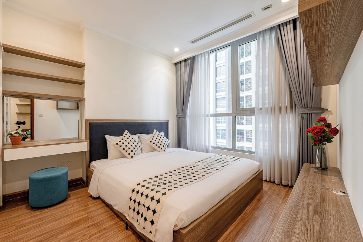 Ein modernes Hotelzimmer mit einem großen Bett, einem Nachttisch, einem Spiegel und einem Fenster mit Vorhängen.
