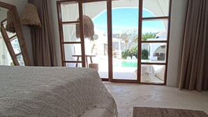 A bedroom with a large bed, a view of a swimming pool, and a sliding glass door leading to an outdoor area. - Sal Central (Pecatu)