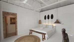 A bedroom with a bed, a bench, a woven rug, and a decorative wall piece. - Sal Central (Pecatu)