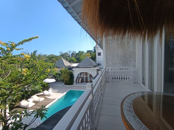 A poolside area with a clear view of a traditional house in the background. - Sal Central (Pecatu)