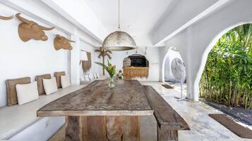 Una habitación amplia con una larga mesa de madera, una lámpara colgante y vistas a un exuberante jardín a través de un arco.