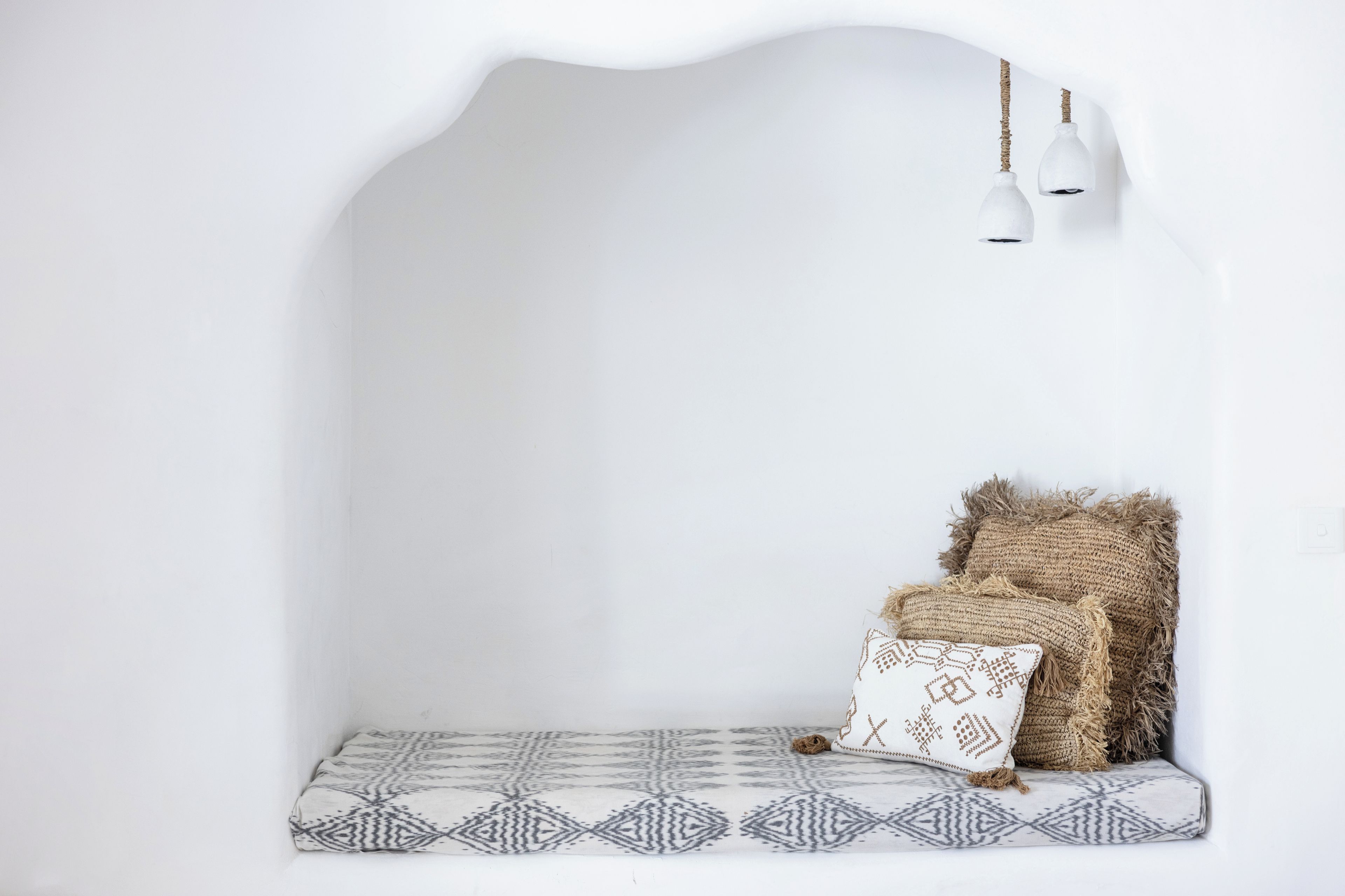 Habitación minimalista con pared blanca, un cojín estampado y dos lámparas colgantes.