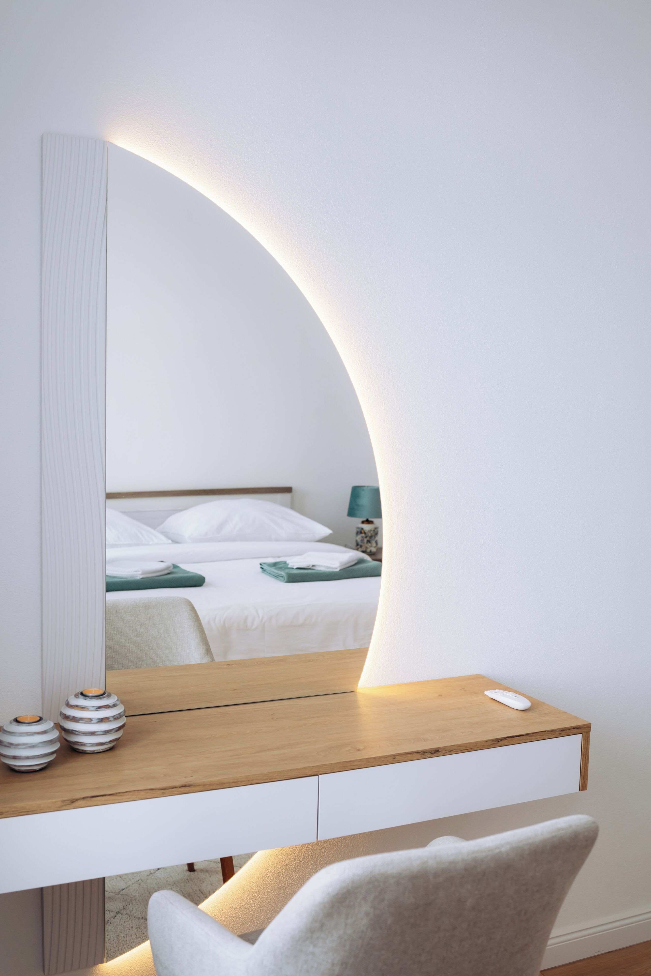 Un dormitorio moderno con cama, mesita de noche y un espejo grande con marco curvo.