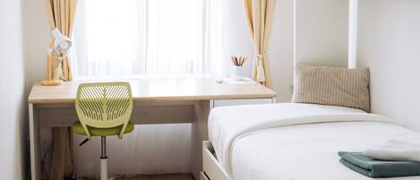 A bedroom with a bed, desk, chair, and a window with curtains.