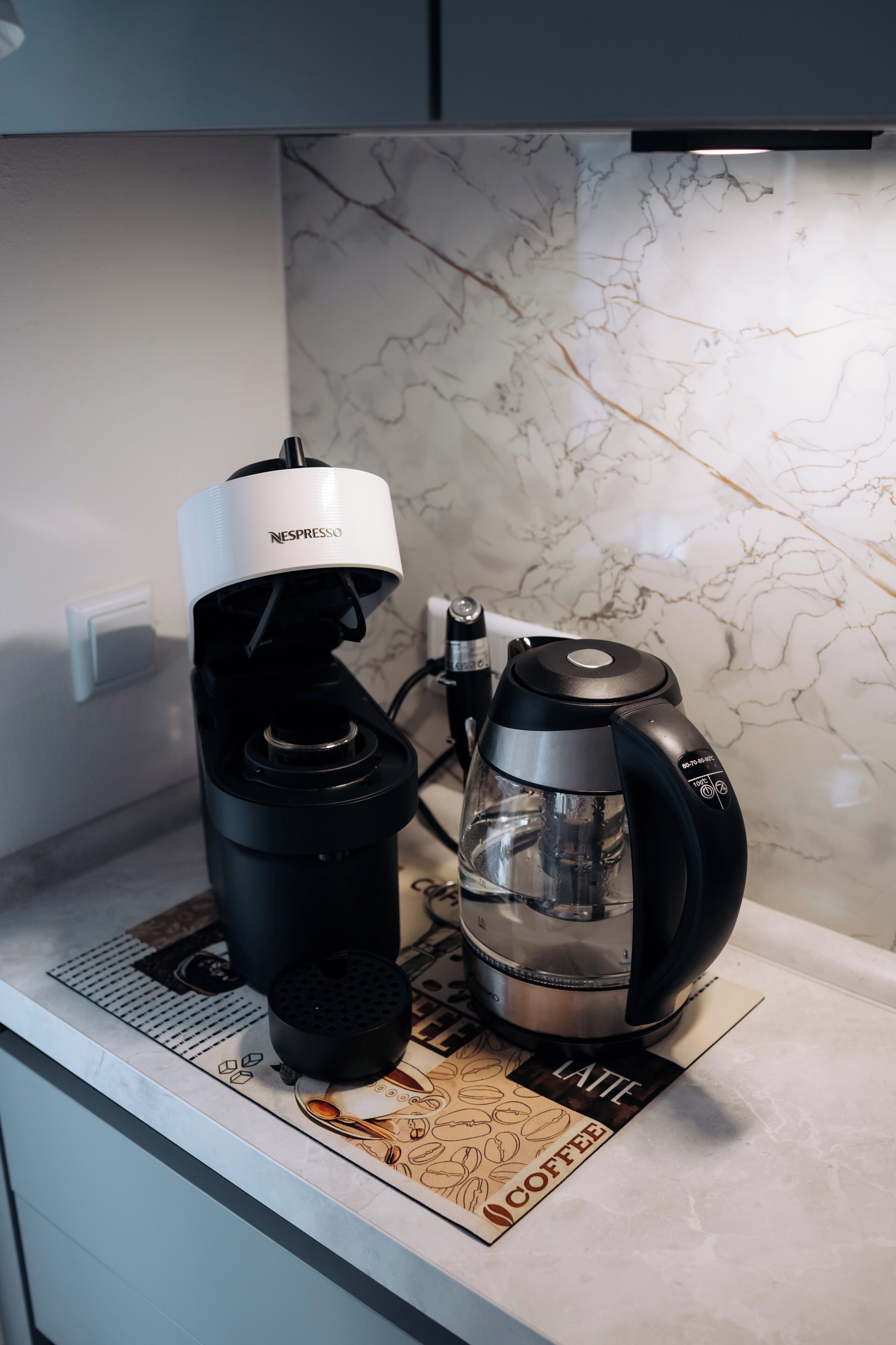 A coffee machine and a kettle on a kitchen counter with a marble backsplash.