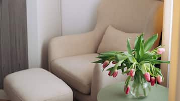 A corner room with a beige sofa, a small round table, and a vase with flowers.