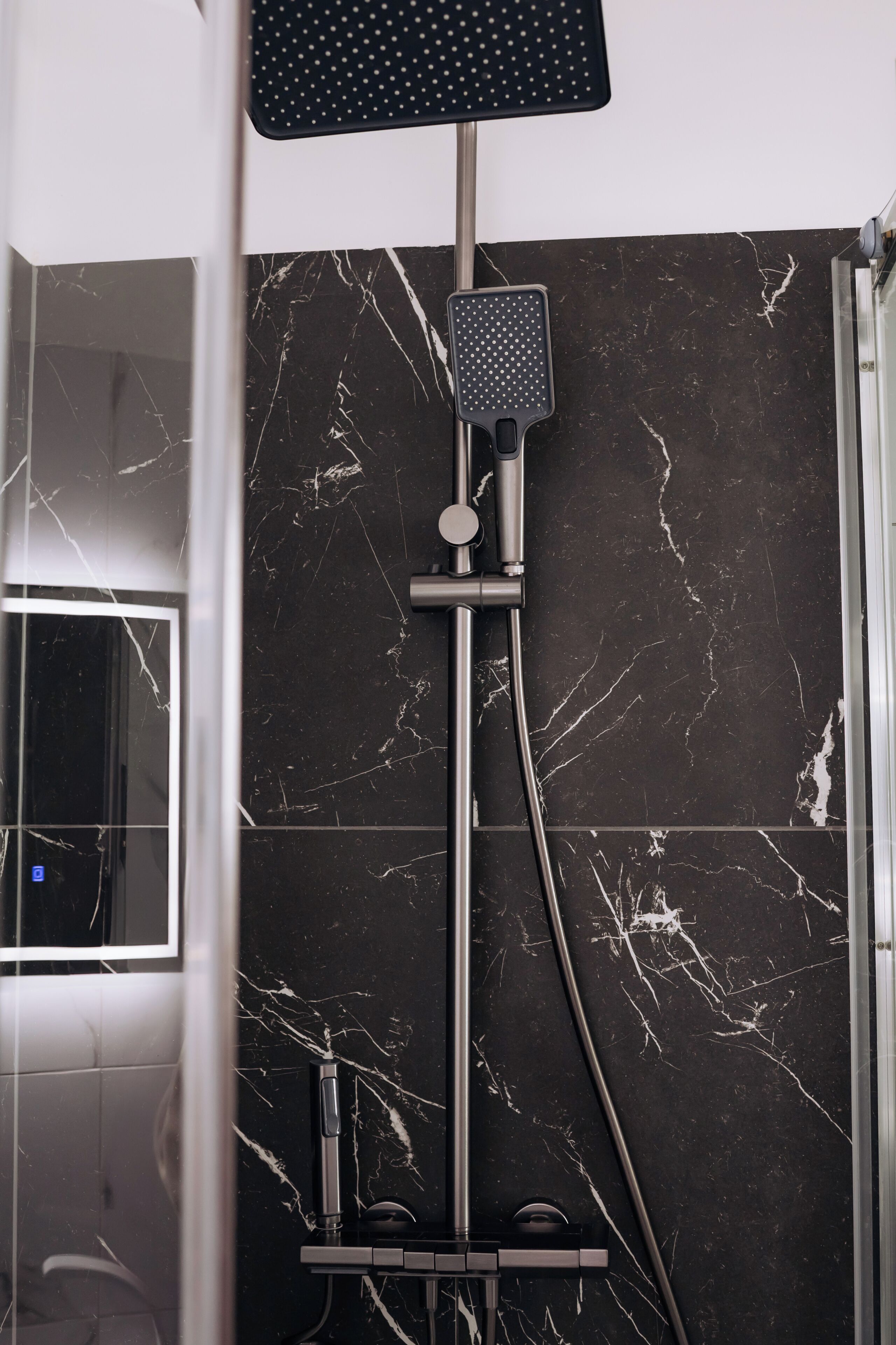 A shower with a handheld showerhead, a wall-mounted control panel, and a glass door.