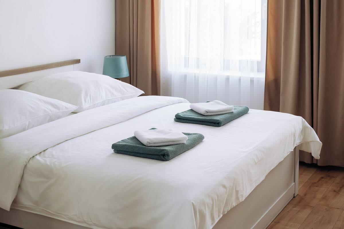 Una habitación de hotel con una cama, una mesita de noche, una lámpara y una ventana con cortinas.