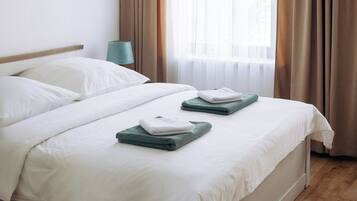 A hotel room with a bed, a nightstand, a lamp, and a window with curtains.