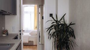 Una cucina moderna con zona pranzo, un'ampia pianta in vaso e vista su una camera da letto attraverso una porta aperta.