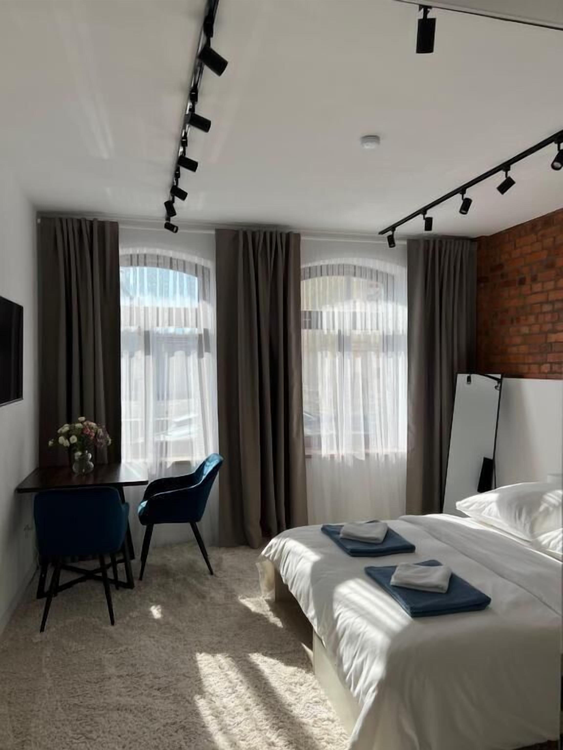 A hotel room with a bed, a desk, a chair, and a large window with curtains.