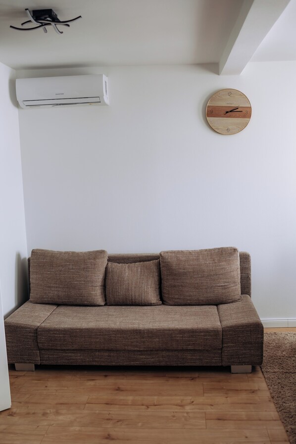 Ein braunes Sofa vor einer weißen Wand, mit einer runden Holz-Uhr und einer Klimaanlage darüber.