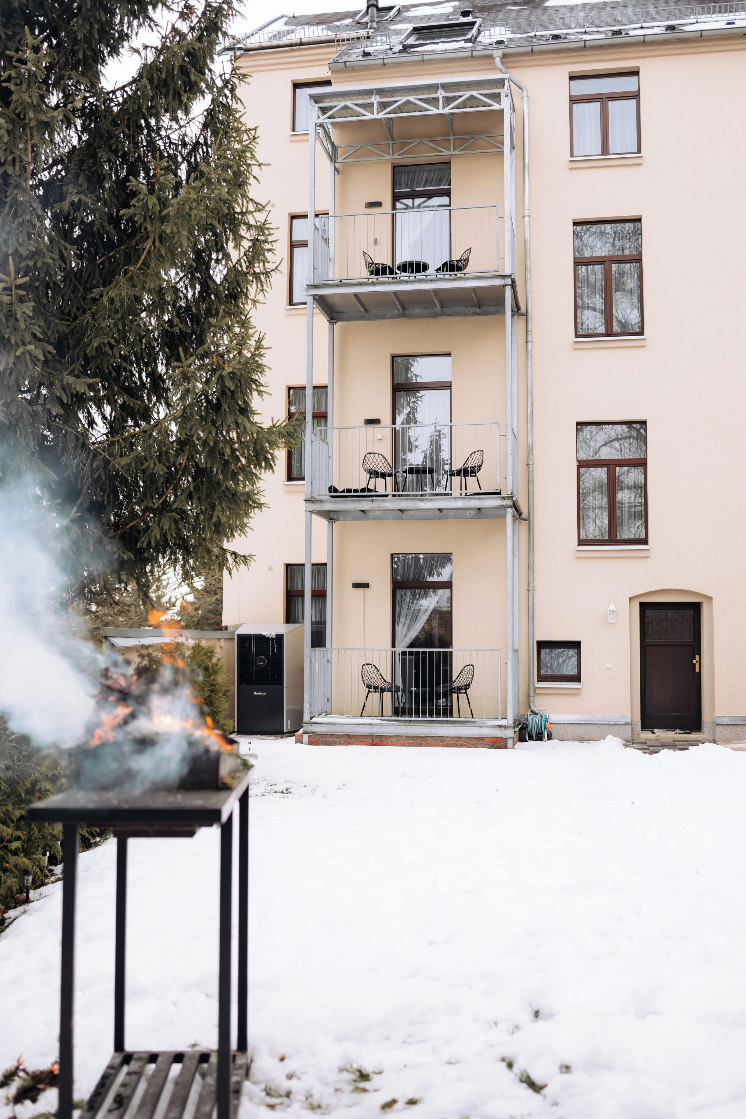Un immeuble à plusieurs étages doté de balcons, d’un barbecue et d’un sol recouvert de neige.