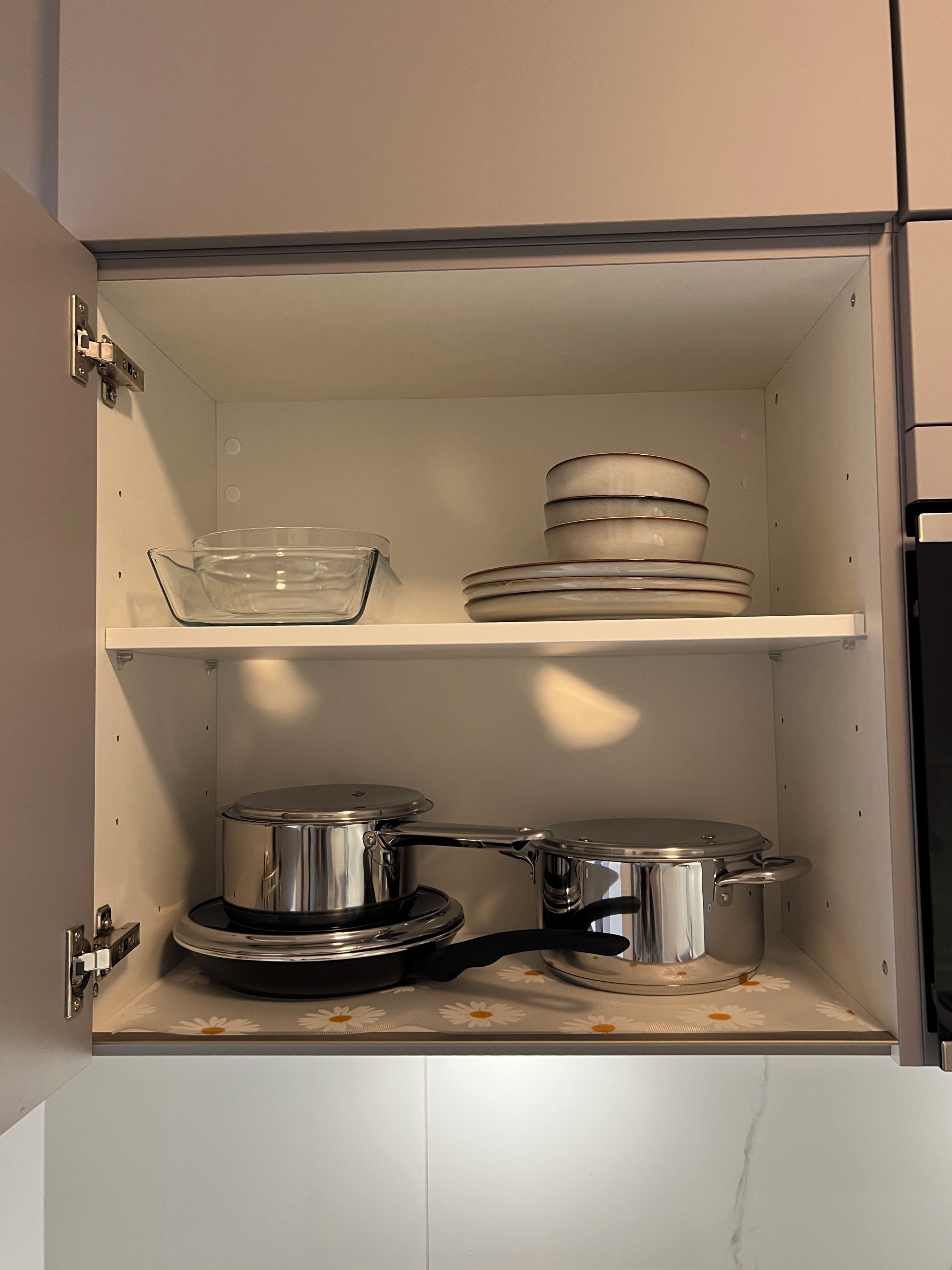 Un meuble de cuisine contenant un récipient en verre transparent, des assiettes empilées et des ustensiles de cuisine en acier inoxydable.