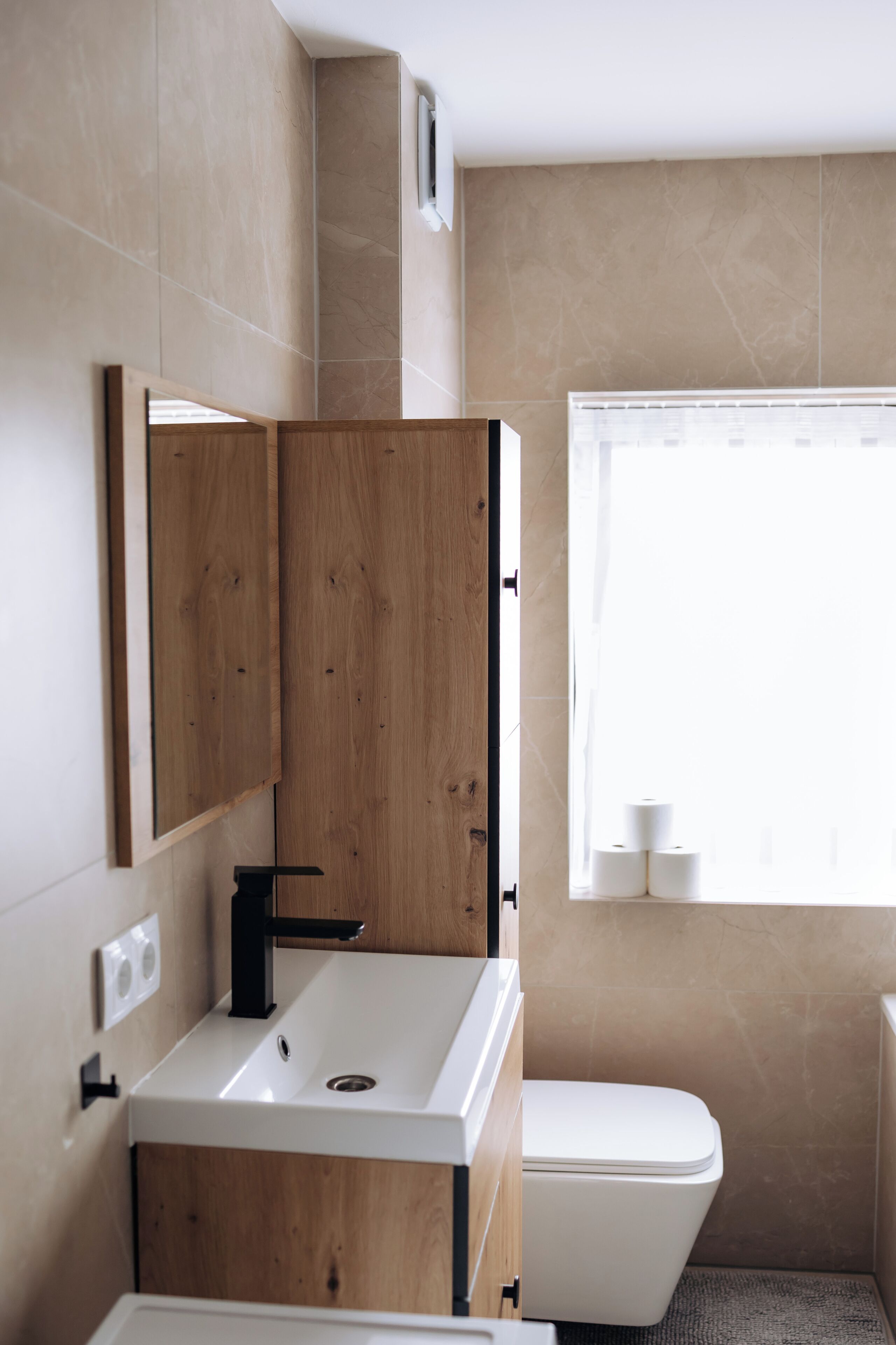 Un baño con tocador de madera, un lavamanos blanco, un inodoro y un ventanal con vistas.