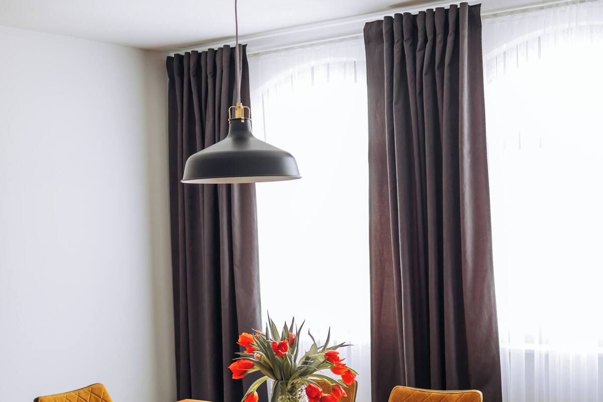 Un comedor con una mesa de madera, cuatro sillas, un florero con flores y una lámpara colgante.