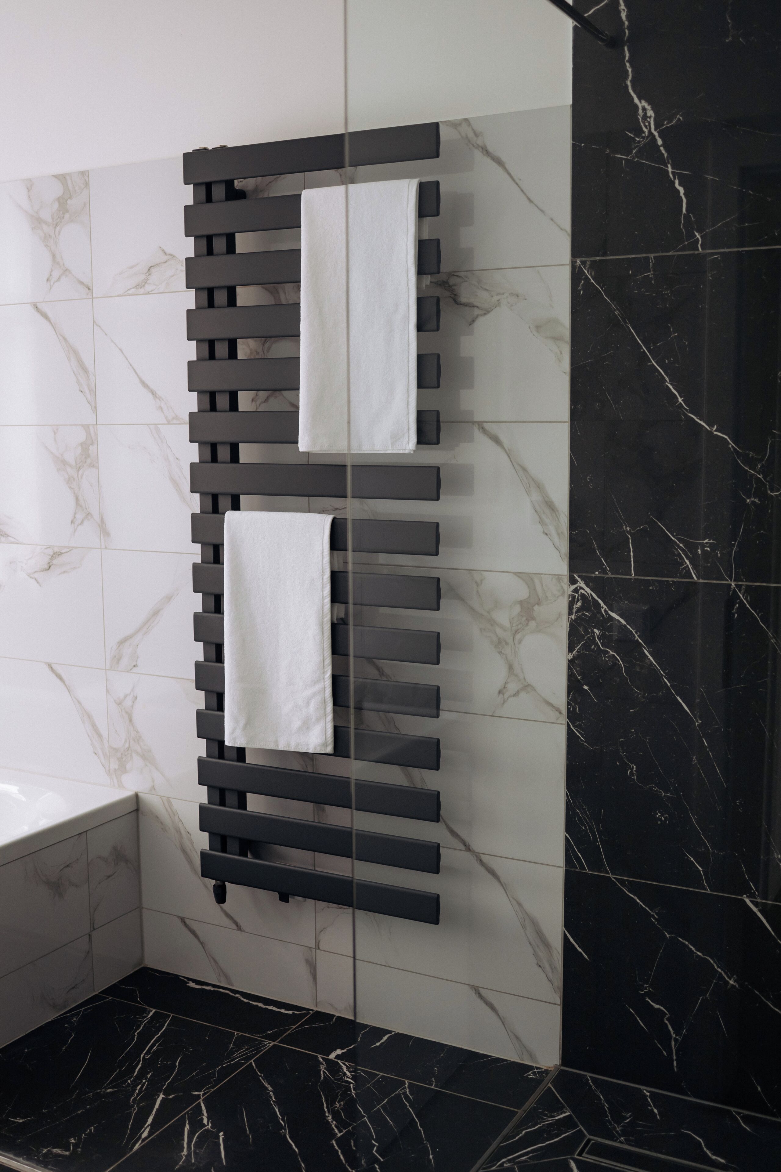 A bathroom with a black and white tiled wall, a black marble floor, and a towel rack with two towels.