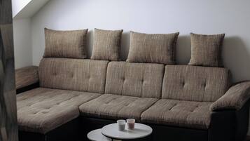 A modern loft bedroom with a sectional sofa, a small round table, and a skylight.