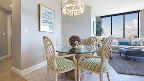 Een eetruimte met een glazen tafel, vier stoelen met gestreepte kussens, een decoratieve dennenappel en een wandlamp.
