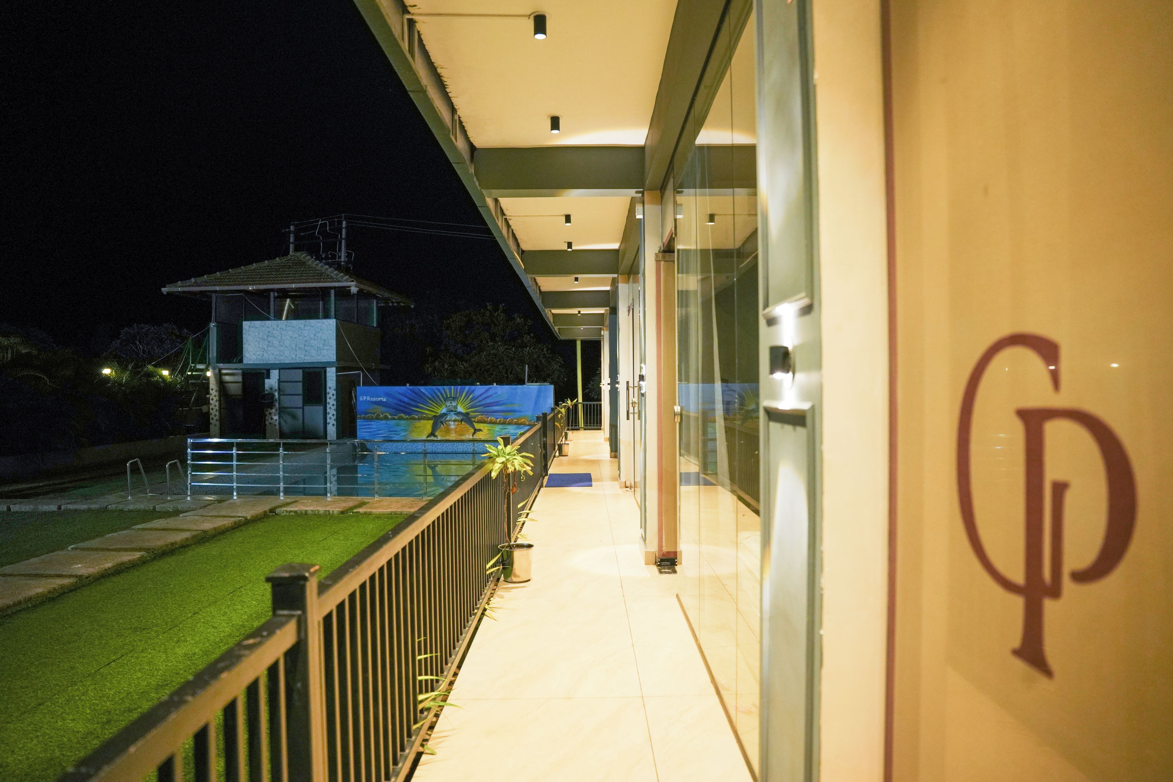A hotel corridor with a pool view, a sign with a monogram, and a glass railing.