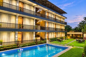 Un hotel de varios pisos con piscina, asientos al aire libre y un jardín bien cuidado.