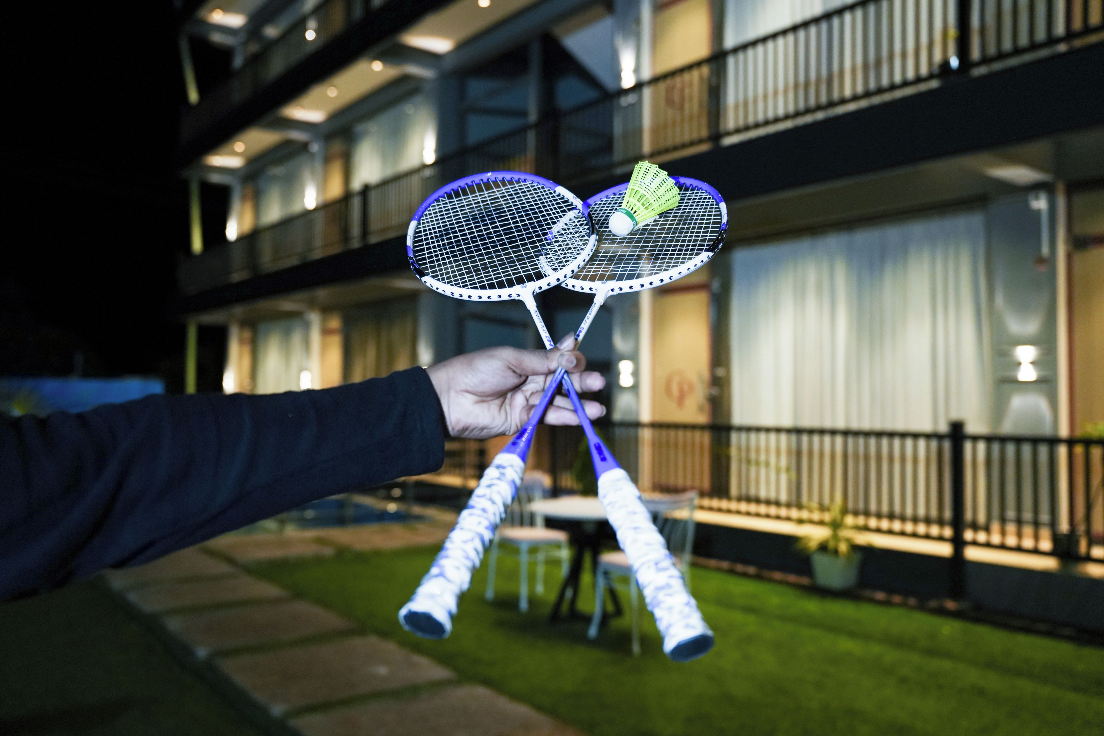 Een hand die badmintonrackets vasthoudt, met een gebouw op de achtergrond.