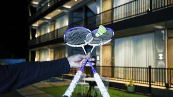 Een hand die badmintonrackets vasthoudt, met een gebouw op de achtergrond.