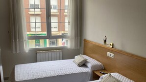 A hotel room with two beds, a window with curtains, a radiator, and a bedside table with a lamp. - HOSTAL LIBERTAD (Villadangos del Paramo)
