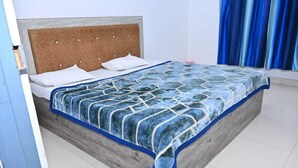 A bed with a wooden headboard, a blue and white patterned bedspread, and white pillows. - NIRMALA GARDEN (Aonla)