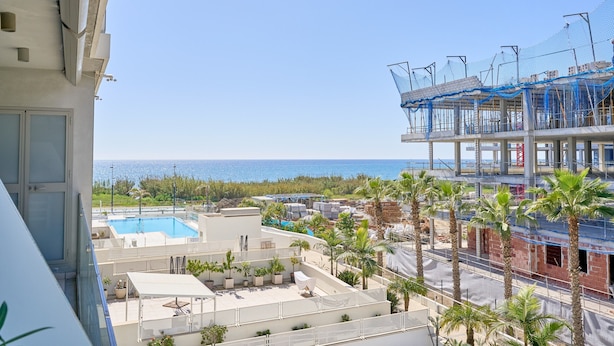 A rooftop pool with a view of the sea, palm trees, and a building under construction. - Apartment 'Sunset Panorama' with Sea View, Wi-Fi and Air Conditioning (El Morche)