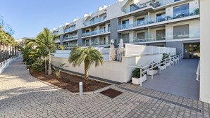 A modern hotel with multiple balconies, a paved walkway, and palm trees. - Apartment 'Sunset Panorama' with Sea View, Wi-Fi and Air Conditioning (El Morche)