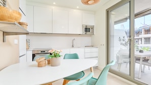 A modern kitchen with white cabinets, a microwave, and a dining area with a white table and teal chairs. - Apartment 'Sunset Panorama' with Sea View, Wi-Fi and Air Conditioning (El Morche)