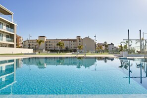 En swimmingpool med klart vatten, omgiven av byggnader och palmer.