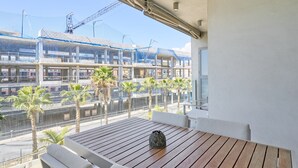 A balcony with a wooden table and white chairs, overlooking a construction site with multiple buildings and palm trees. - Apartment 'Sunset Panorama' with Sea View, Wi-Fi and Air Conditioning (El Morche)