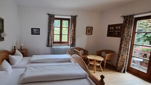 Ein Schlafzimmer mit zwei Betten, einem Fenster mit Vorhängen, einem Sessel und einem kleinen Tisch.