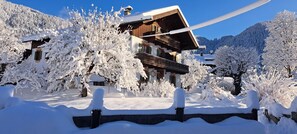 Un chalet en bois doté d’un balcon, entouré d’arbres couverts de neige et avec une chaîne de montagnes en toile de fond.