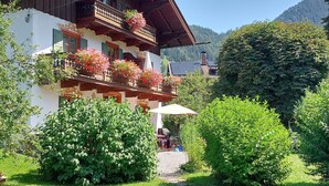 Ein zweistöckiges Gebäude mit Balkonen, einem Garten und einer Bergkulisse.