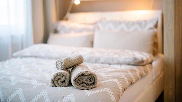 A neatly made bed with rolled towels, a patterned bedspread, and a bedside table with a lamp. - Apartment 'Air Fair' with Wi-Fi (Düsseldorf)