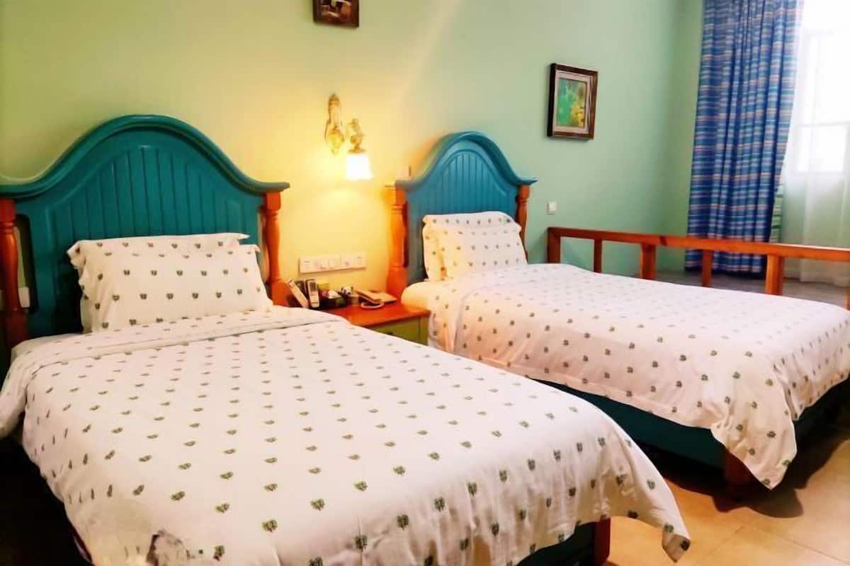 A room with two beds, a nightstand, a lamp, and a window with curtains.