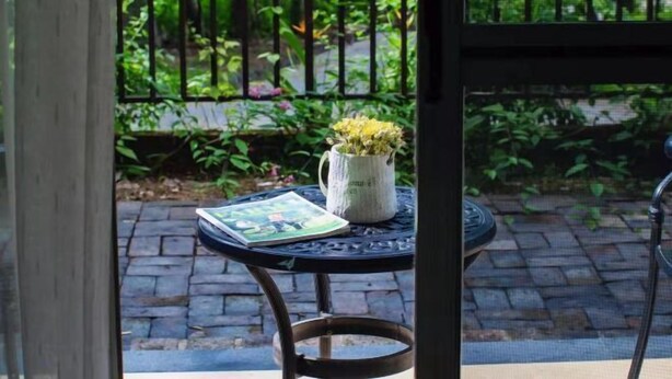 A table with a book and a vase of flowers, set against a garden backdrop. - Forest Inn (Hainan University, Zhangzhou Botanical Garden Thermoscience Academy) (Danzhou)