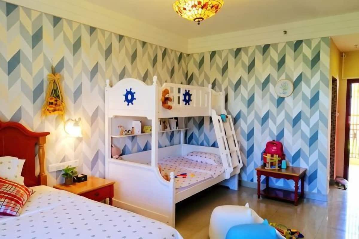 A room with a bunk bed, a bedside table, a lamp, and a wall with a geometric pattern.