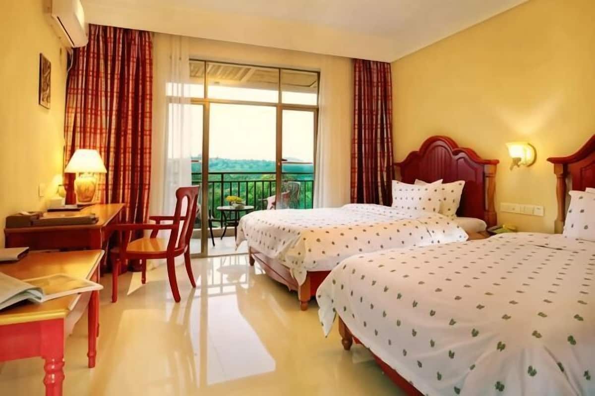 A hotel room with two beds, a desk, a chair, a balcony with a view, and a window with curtains.
