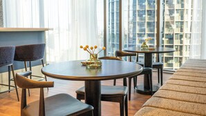 A modern dining area with round tables and chairs, a bar counter, and large windows offering a city view. - Queen's Wharf 1B+Study · City Breeze & Views (Brisbane City)
