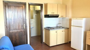 A compact kitchen with a built-in stove, sink, and white refrigerator. - Charming 19 sq m studio apartment.It features a fully equipped kitchenette, a double bed or two single beds, and a private bathroom with shower, bidet, and hairdryer. The apartment also boasts an outdoor space with a sea view, a patio or terrace, and a t (Stintino)