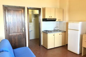 A compact kitchen with a built-in stove, sink, and white refrigerator. - Charming 19 sq m studio apartment.It features a fully equipped kitchenette, a double bed or two single beds, and a private bathroom with shower, bidet, and hairdryer. The apartment also boasts an outdoor space with a sea view, a patio or terrace, and a t (Stintino)
