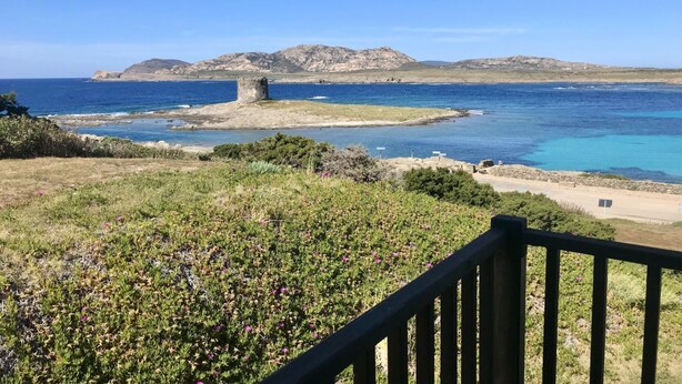A coastal landscape with a stone structure, clear blue sea, and distant hills. - Charming 19 sq m studio apartment.It features a fully equipped kitchenette, a double bed or two single beds, and a private bathroom with shower, bidet, and hairdryer. The apartment also boasts an outdoor space with a sea view, a patio or terrace, and a t (Stintino)