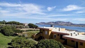 A coastal building with a flat roof, surrounded by greenery and a view of the sea. - Charming 19 sq m studio apartment.It features a fully equipped kitchenette, a double bed or two single beds, and a private bathroom with shower, bidet, and hairdryer. The apartment also boasts an outdoor space with a sea view, a patio or terrace, and a t (Stintino)