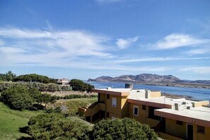 A coastal building with a flat roof, surrounded by greenery and a view of the sea. - Charming 19 sq m studio apartment.It features a fully equipped kitchenette, a double bed or two single beds, and a private bathroom with shower, bidet, and hairdryer. The apartment also boasts an outdoor space with a sea view, a patio or terrace, and a t (Stintino)