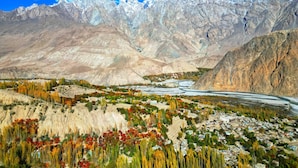 A mountainous landscape with a river, a small settlement, and snow-capped peaks.